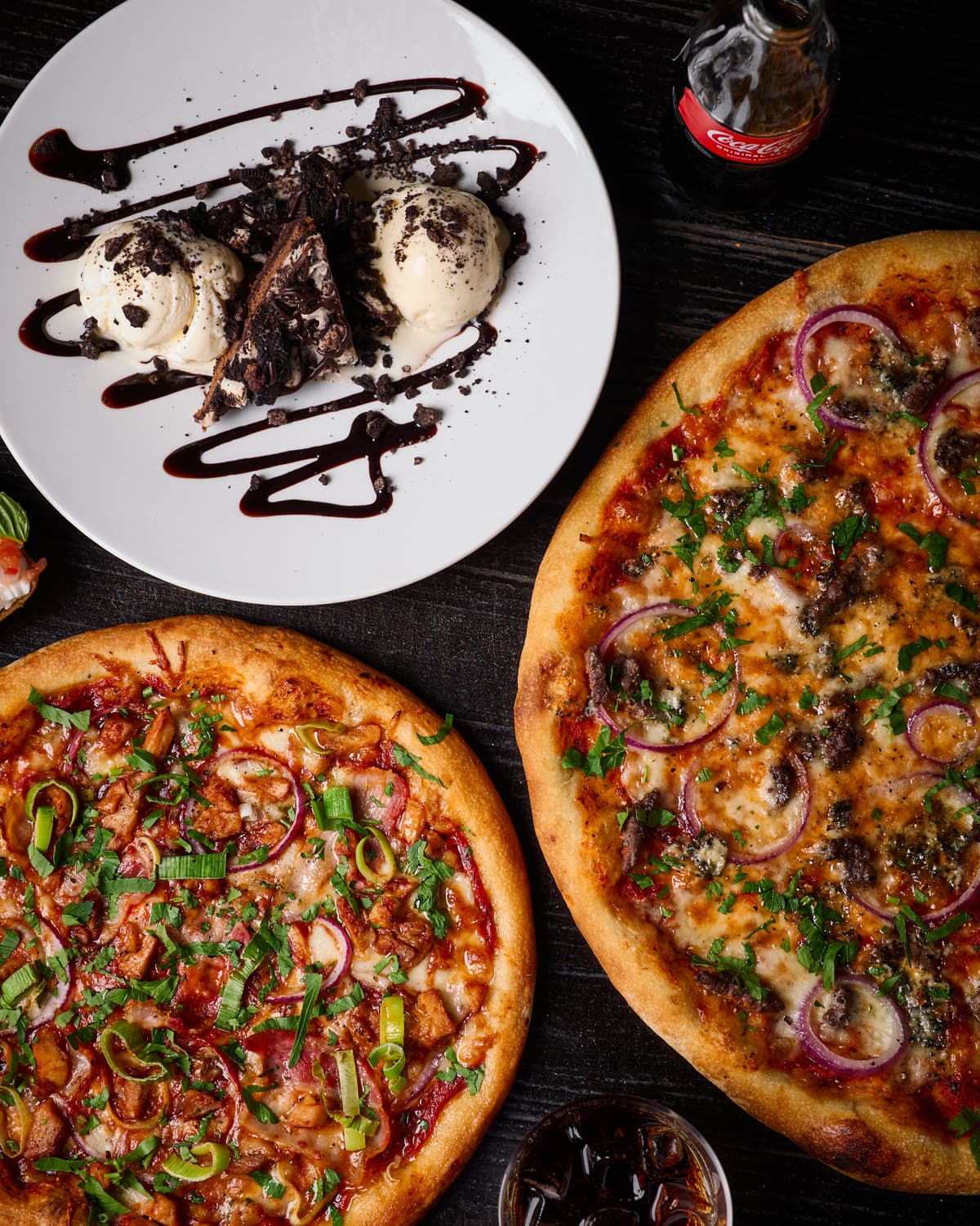 To pizzaer og en dessert på et bord, fotografert for Peppes Pizza.