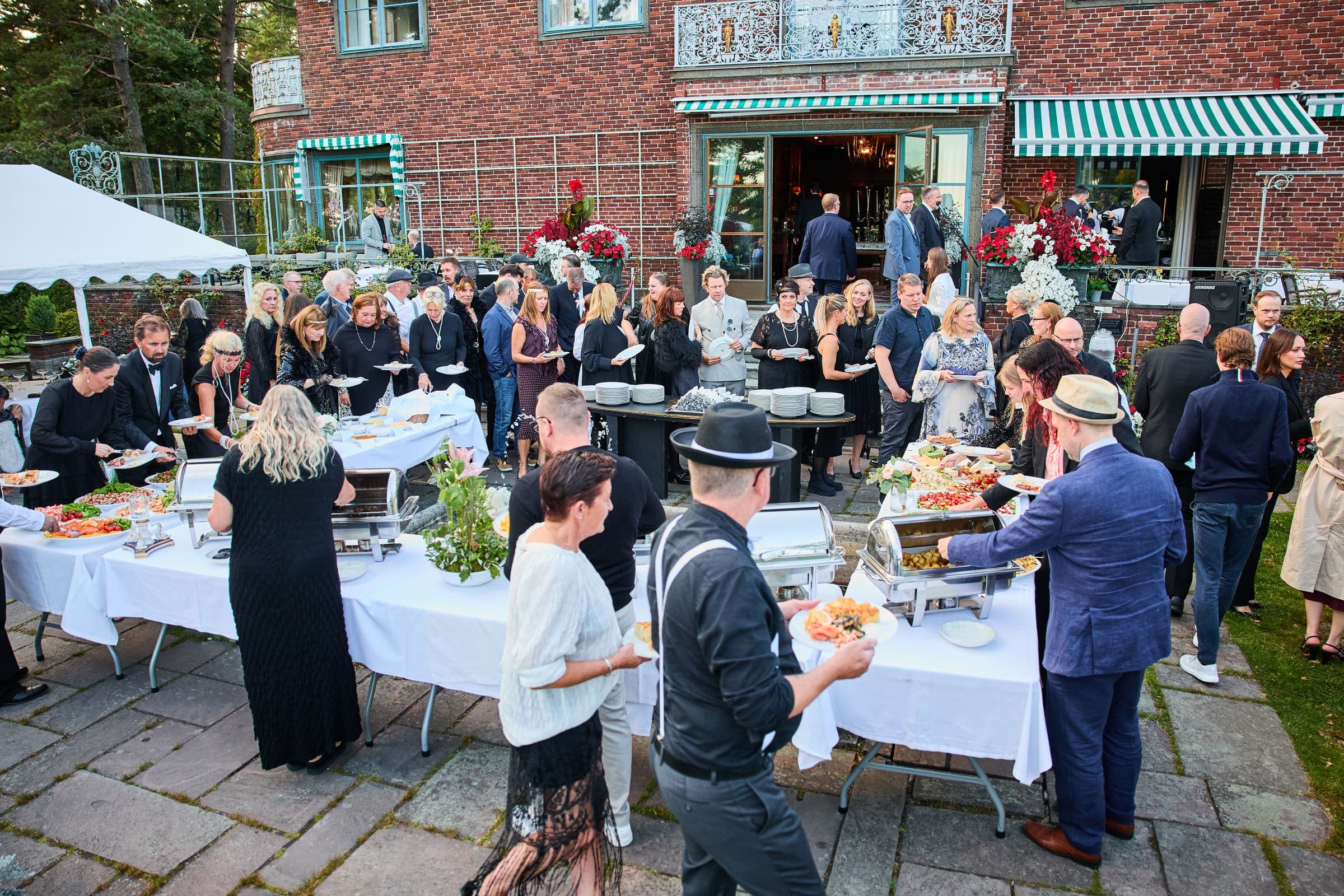 Gjester i kø ved buffeten utenfor en murvilla under et firmaarrangement