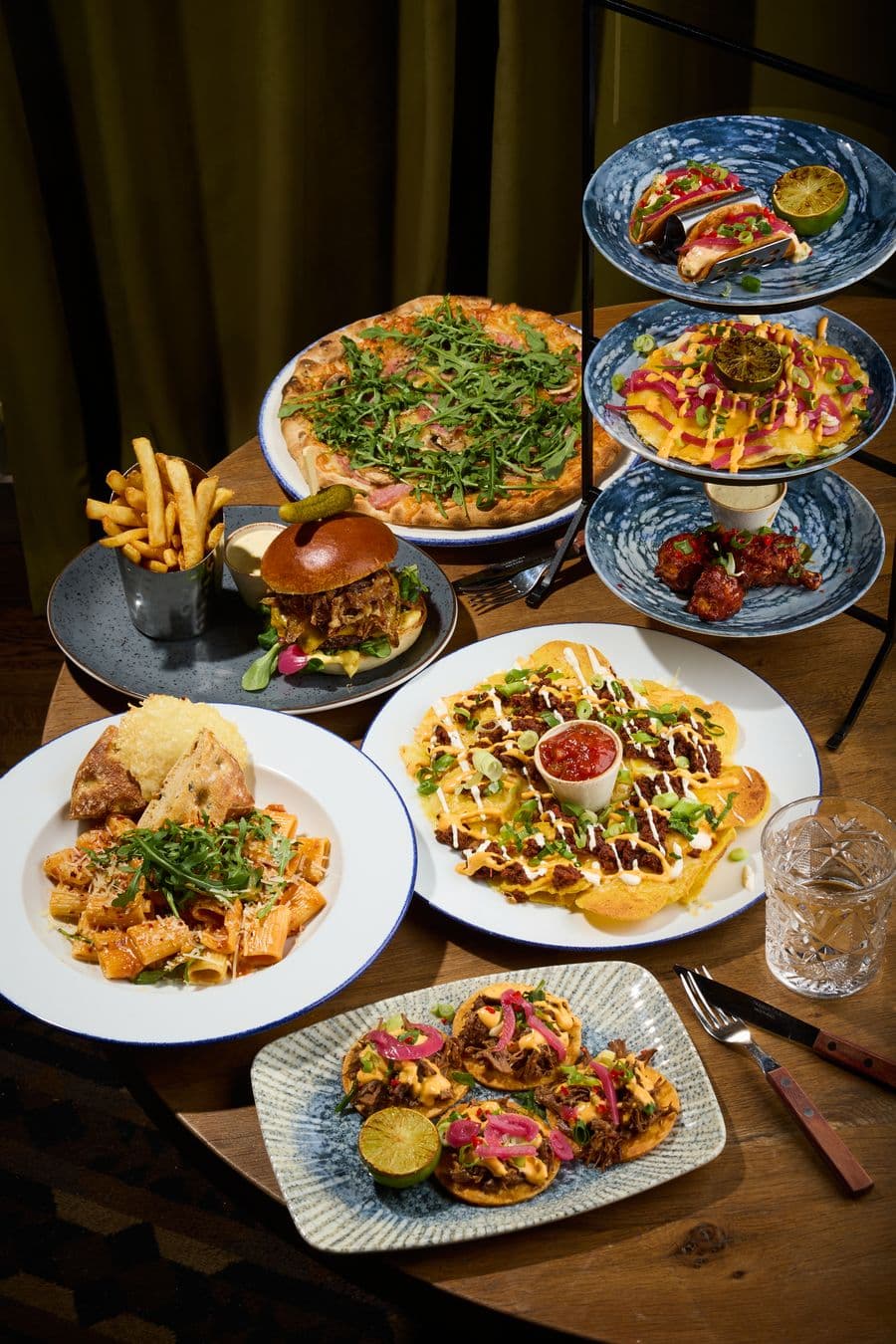 Bord dekket med retter fra Egons meny: pizza, burger, pasta, nachos, tacos og pommes frites