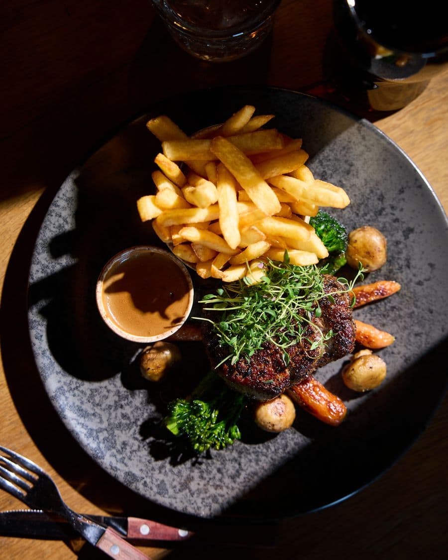 Biff med pommes frites, brokkoli og saus på en mørk tallerken